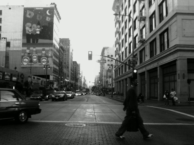 One of the first rules photography students learn is never shoot people with something sticking out of their head.  However in this case, the alignment of the pedestrian with the traffic light pole perfectly balances the frame